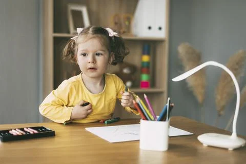 A little girl draws at the table with colored pencils at home or in kindergarten Stock Photos