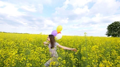 Little girl in a dress running through yellow wheat field with balloons in hand Stock Footage