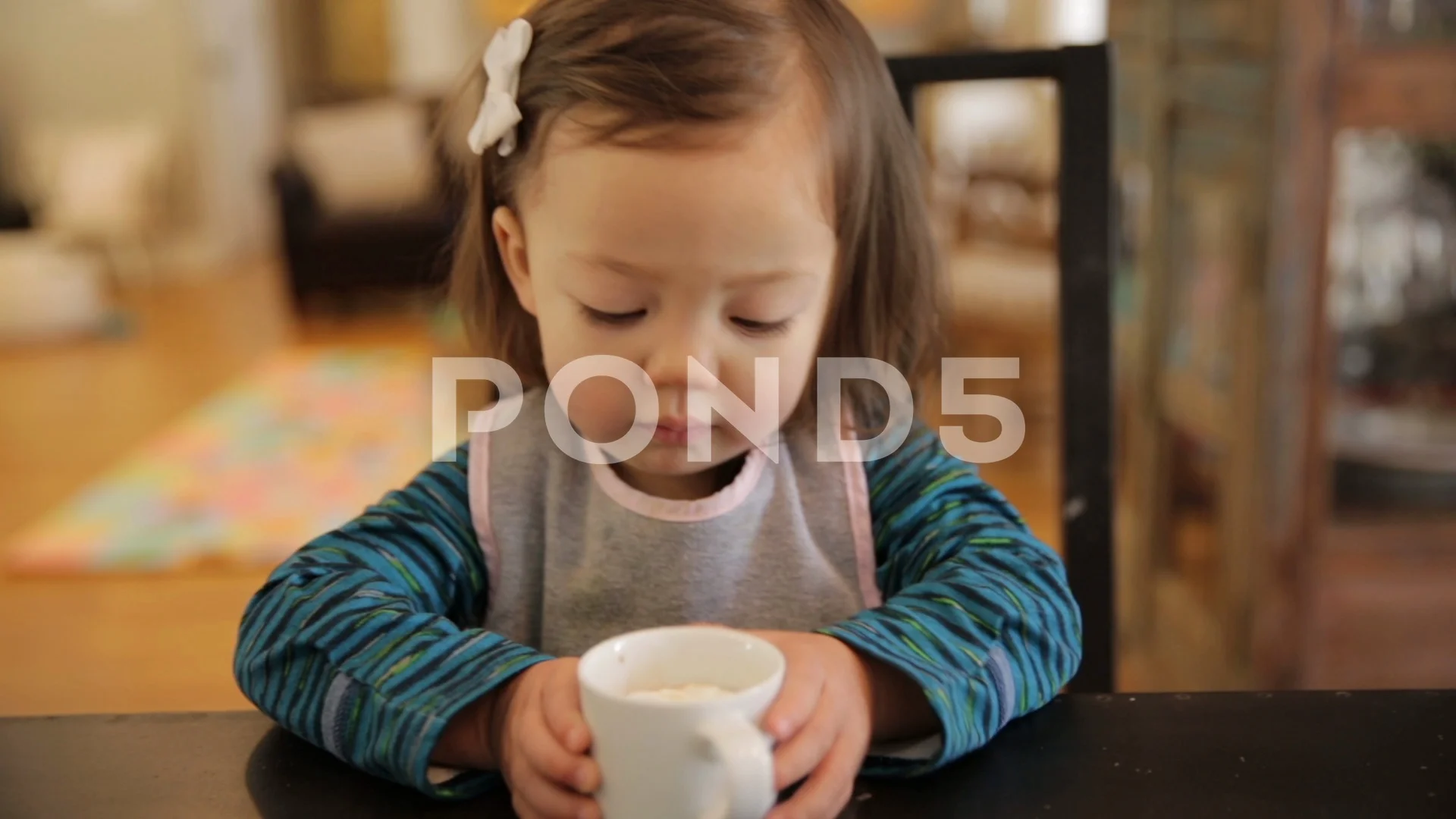 Little Girl Drinking Hot Chocolate Out of Small White Mug on Table