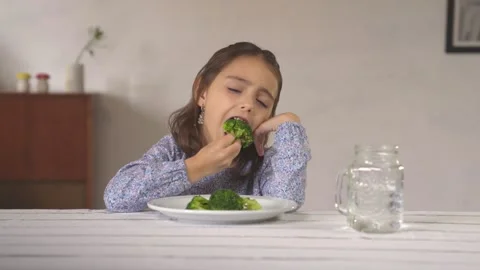 Little girl eates with mistrust a broccoli, then she likes it. Stock Footage 241042657