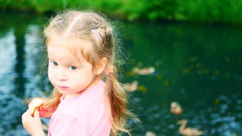 Little girl eats bread and feeds ducks near the pond Video stock 115507086