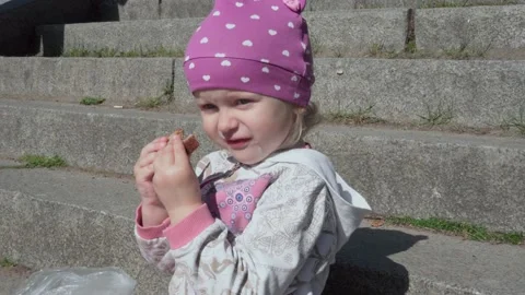 A little girl eats bread while sitting on the stone steps. Stock Footage 141316616