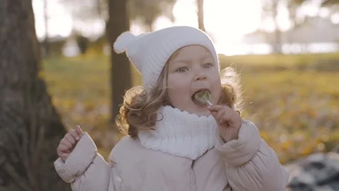 A little girl eats a candy on a stick in park. Kid with candy. Happy baby face Stock-Footage 223689722