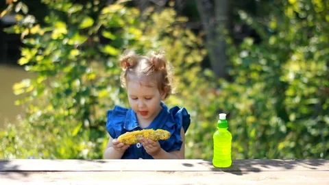 A little girl eats corn and drinks lemonade. Picnic Stock Footage 77998726