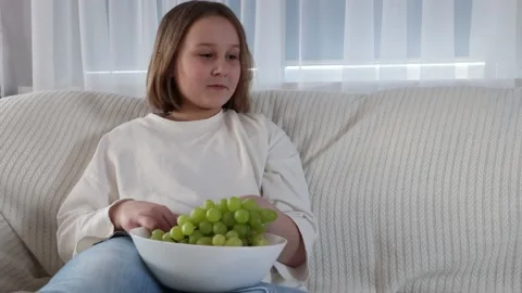 A little girl eats grapes on the couch, healthy eating. Stock Footage 153753565