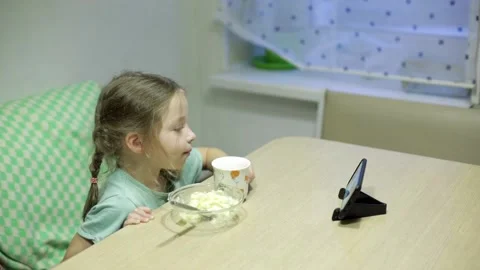 A little girl eats mashed potatoes and watches cartoons on her smartphone Stock Footage 143897074