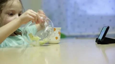 A little girl eats mashed potatoes and watches cartoons on her smartphone 스톡 동영상 143897083