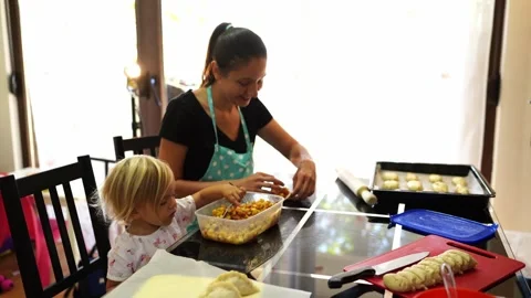 Little girl eats the stuffing with a spoon next to her mother stuffing pies Stock-Footage 280209019