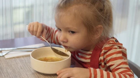 The little girl eats vegetable soup. She sits at the table and holds a spoonful Stock Footage 102520732