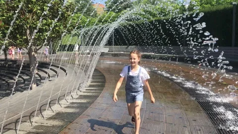 A little girl has fun between splashes of water in a fountain on the street. It' Stock Footage 264802422