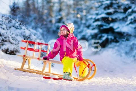 Little girl having fun on a sledge in snowy winter forest Stock Photos