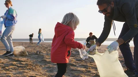 Little girl helps her parents to clean up area of dirty beach with garbage bags Stock Footage