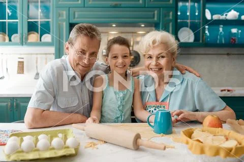 Little girl with her grandparents cooking at the kitchen Stock Photos