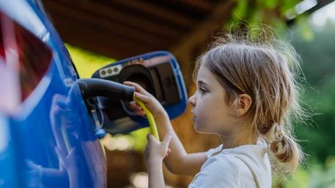 Little girl holding power supply cable and charging their electric car. Stock Photos