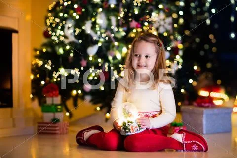 Little girl holding snow globe under Christmas tree Stock Photos
