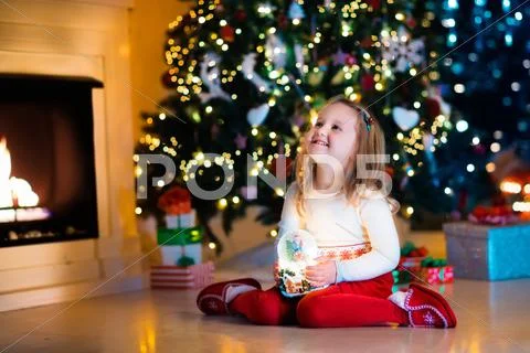 Little girl holding snow globe under Christmas tree Stock Photos
