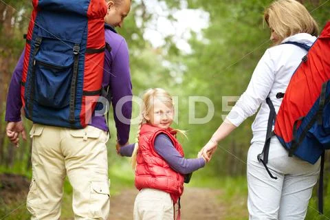 Little girl looking at camera with her parents walking outdoors Stock Photos