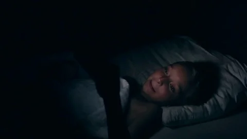 Little girl is looking smartphone lying in bed at night. Girl cries while Stock Footage