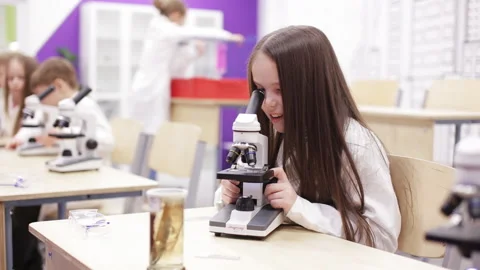 Little girl is looking through a microscope at a lesson in school Video stock 86801448