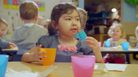 A little girl looks at the camera while eating her snack and makes funny faces Stock Footage 34005244