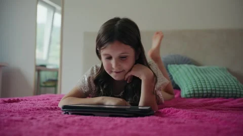 Little Girl Lying on Bed Using Digital Tablet at Home Vidéo 343879279