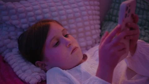 Little Girl Lying in Bed Using Smartphone at Night in Dim Light Stock Footage 345528206
