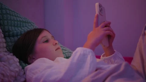 Little Girl Lying in Bed Using Smartphone at Night Stock Footage 345528328