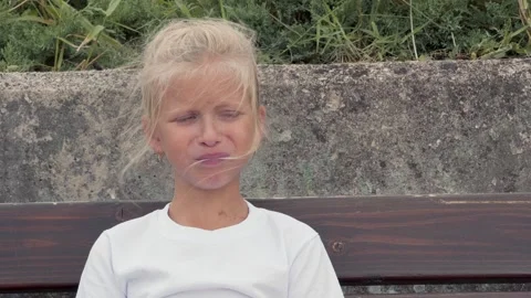 Little girl is making a face while sitting on a bench. Emotional feelings. Stock Footage 251923976