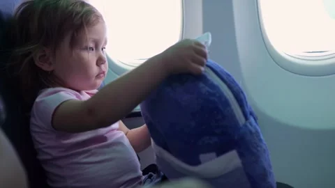 Little girl opens tiny soft backpack sitting by window in airplane Stock Footage 302150462