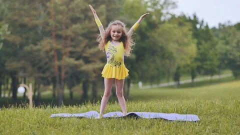 A little girl performs the elements of rhythmic gymnastics in the park. Fotos Stock