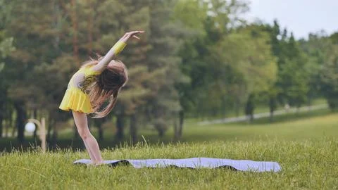 A little girl performs the elements of rhythmic gymnastics in the park. Stock Photos
