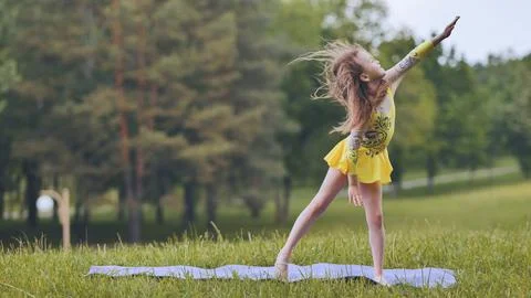 A little girl performs the elements of rhythmic gymnastics in the park. Fotos Stock