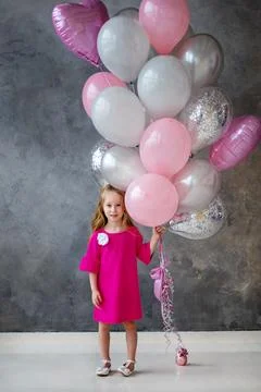 Little Girl in pink dress with pink, grey balloons on grey background. Beauti Stock Photos