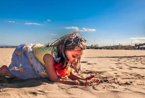Little girl playing at beach bending down on sand happy and free Stock Photos
