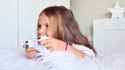 A little girl is playing a computer console on a sofa in a bright room. Video stock 138215401