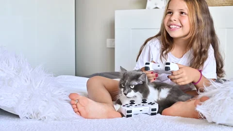 A little girl is playing a computer console on a sofa in a bright room. Video stock 138215749