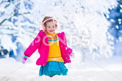 Little girl playing snow ball fight in winter park Stock Photos