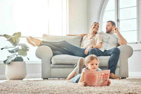 Little girl reading storybook while lying on carpet at home. Smart kid reading Stock Photos