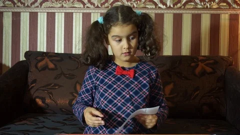 A little girl reads a sheet of paper with a test homework, which she received Stock Footage