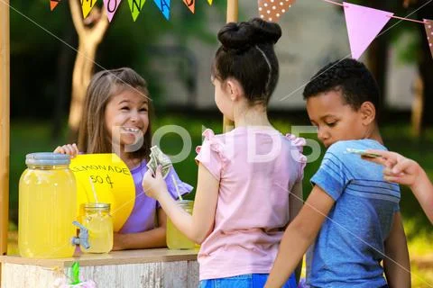 Little girl selling natural lemonade to kids in park. Summer refreshing drink Stock Photos