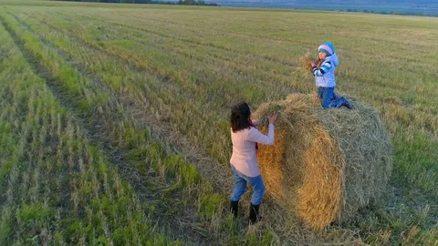 Little girl sits on the stack and throw straws to her mom. Vídeo Stock 85666337