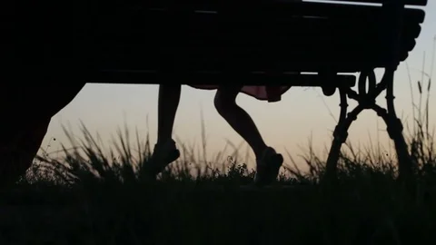 Little Girl Sitting on a Bench Feet Sunset Backlit Silhouette Stock Footage