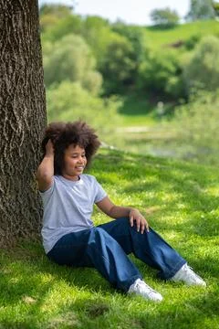 Little girl sitting on grass under tree resting in nature enjoying freshair. Stock Photos