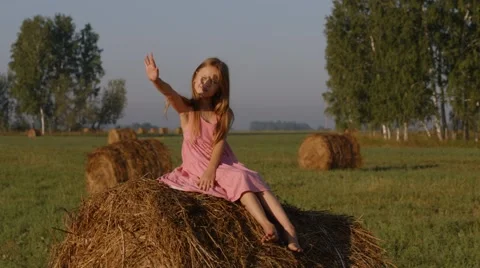 Little girl sitting on a haystack and looking at the sun Video stock 44448945