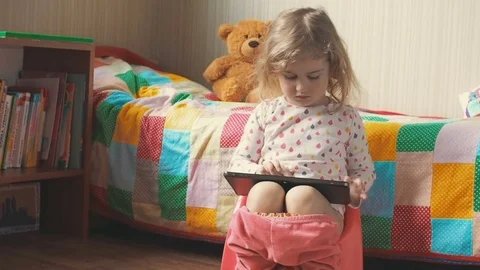 Little girl sitting on the potty beside the bed and playing on a tablet PC. Stock Footage