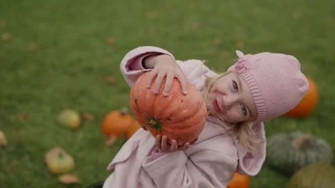 Little girl smiles while holding a pumpkin in a field full of autumn harvest Stock Footage 318156053