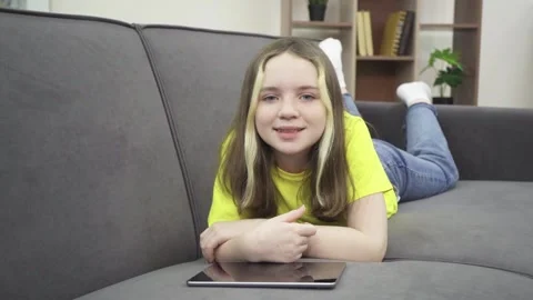 A little girl is smiling while lying on the couch with a tablet. Stock Footage 166196992