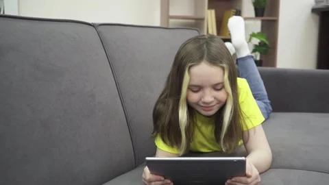 A little girl is smiling while lying on the couch with a tablet. 動画素材 170657616