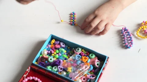 A little girl is stringing beads on a string to create a bracelet Stock Footage 159977716