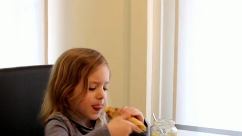Little girl in striped dress sitting at a table, eating pancakes with apple mous Stock Footage